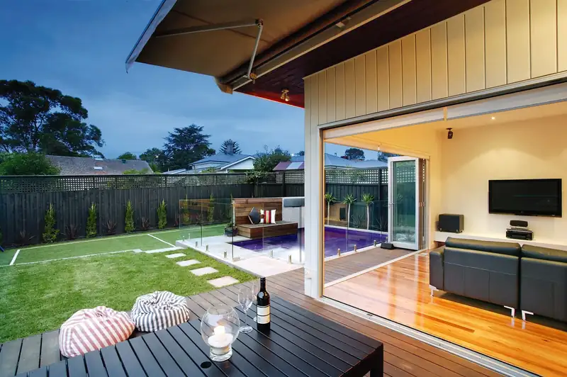 Open-plan living room opening onto a timber deck and lawn at dusk