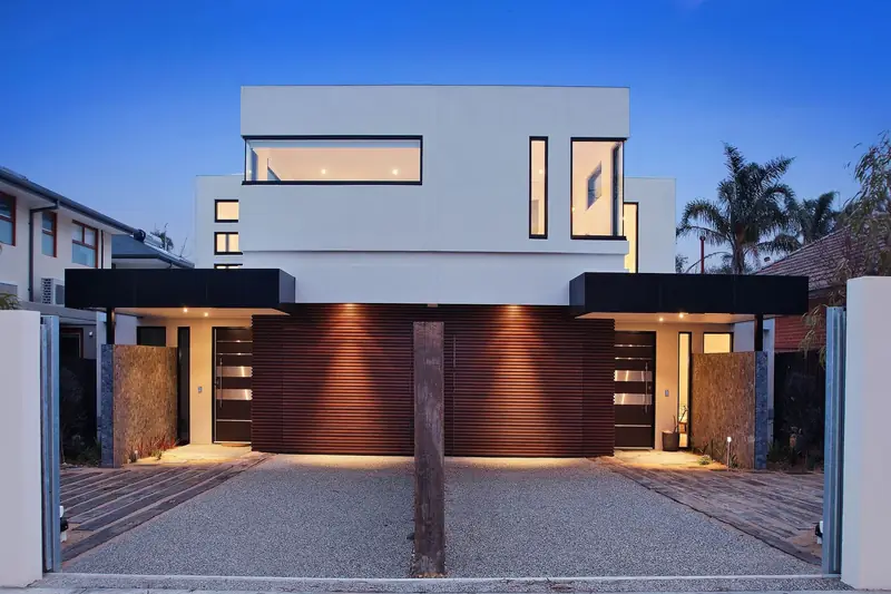 Three-storey contemporary home with timber garage doors at dusk