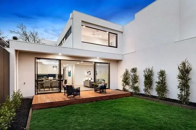 Rear of a white two-storey home opening onto a timber deck and lawn